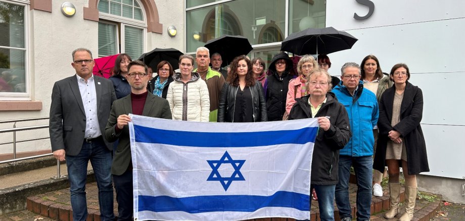 18 Personen stehen vor dem Rathaus Eltville und halten eine Flagge Israels vor sich.