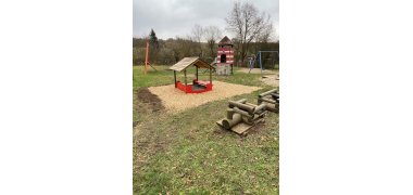 Geräte auf einem Spielplatz: Überdachtes Häuschen, Volleyballnetz, Spielturm, Holzgeräte, Schaukel