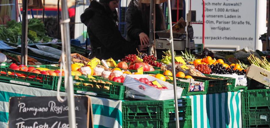 An einem Stand verkauft eine Frau frisches Obst und Gemüse.